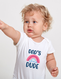 Child wearing a white t-shirt with 'Dad's Little Dude' text and rainbow design on a plain background