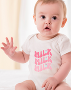 Baby wearing a white onesie with pink text, sitting on a white surface.