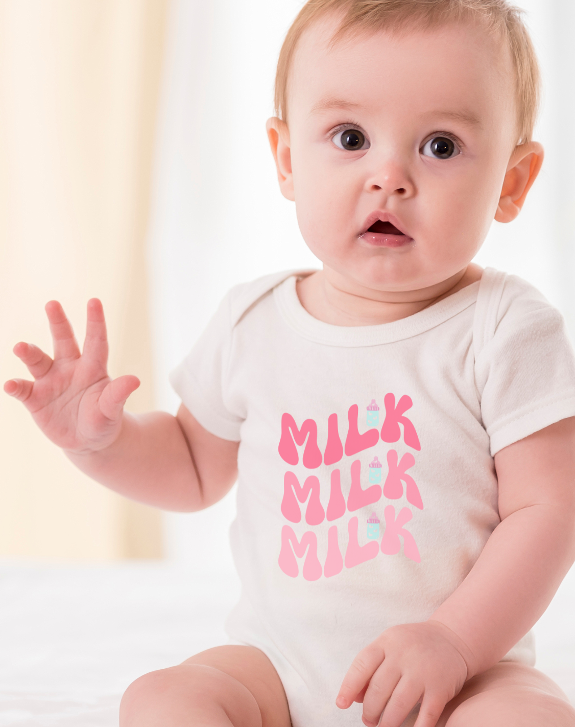 Baby wearing a white onesie with pink text, sitting on a white surface.