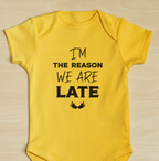 Yellow baby onesie with text I'm the reason we are late on a wooden surface