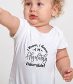 Baby wearing a white onesie with text "I know I'm absolutely adorable" on a plain background
