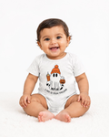 A smiling baby sitting on a white fluffy rug wearing a white short-sleeve bodysuit with a cartoon ghost graphic holding an orange pumpkin and drink, with the text 'I CAN DO TOO-TROUBLE' below.