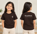 Indian girl wearing a dark brown premium cotton kids’ T-shirt with the Sanskrit shlok Vidya Dadati Vinayam printed on the back.
