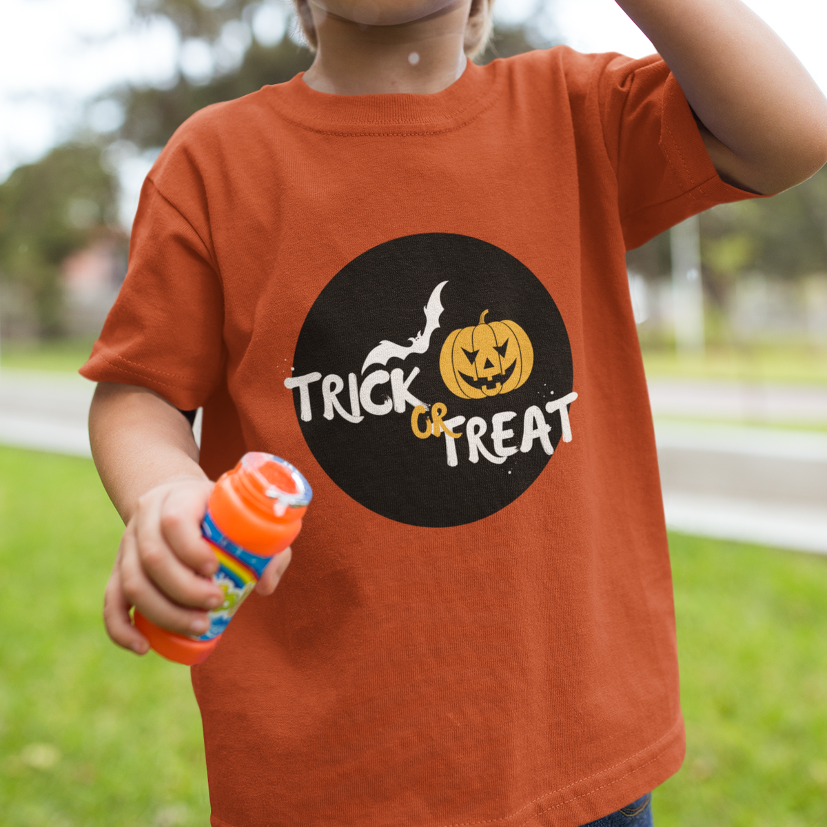 Child blowing bubbles wearing an orange 'Trick or Treat' shirt outdoors.