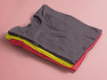 Stack of folded tank tops in gray, yellow, and red on a pink background