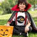 Child in Halloween costume with red cape and 'Trick or Treat' shirt sitting on grass.