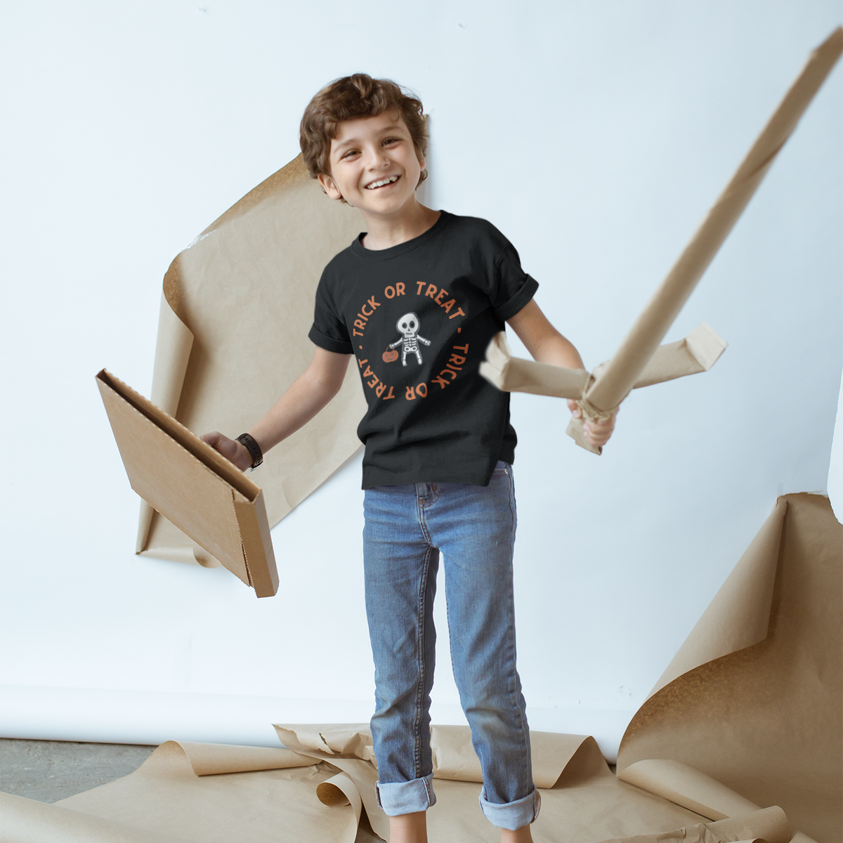 Child wearing a black t-shirt with a graphic design, standing on a white floor with brown paper around.