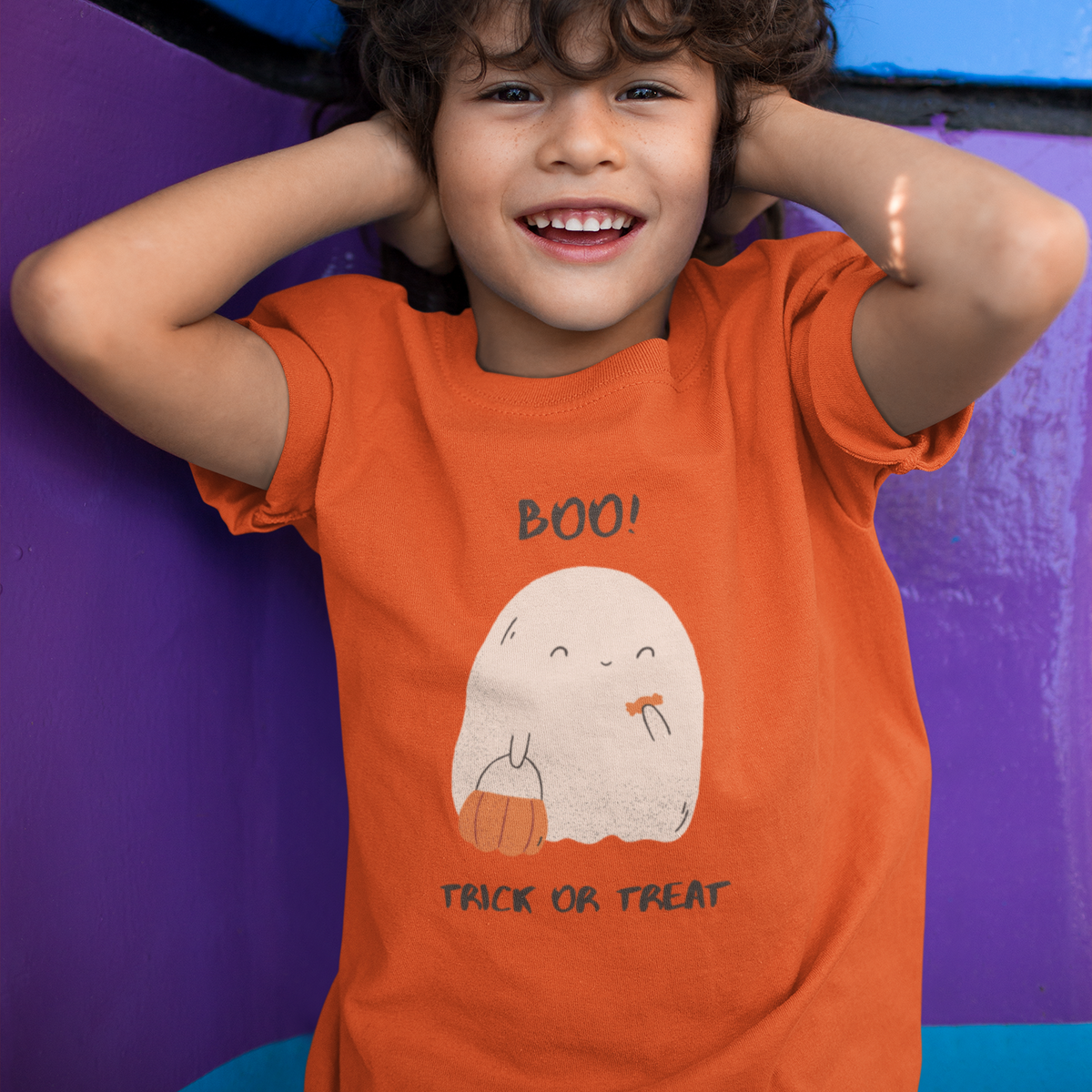 Child wearing an orange 'Boo! Trick or Treat' shirt against a colorful background