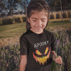Child wearing a black t-shirt with a Halloween design in a field of tall grass and flowers.