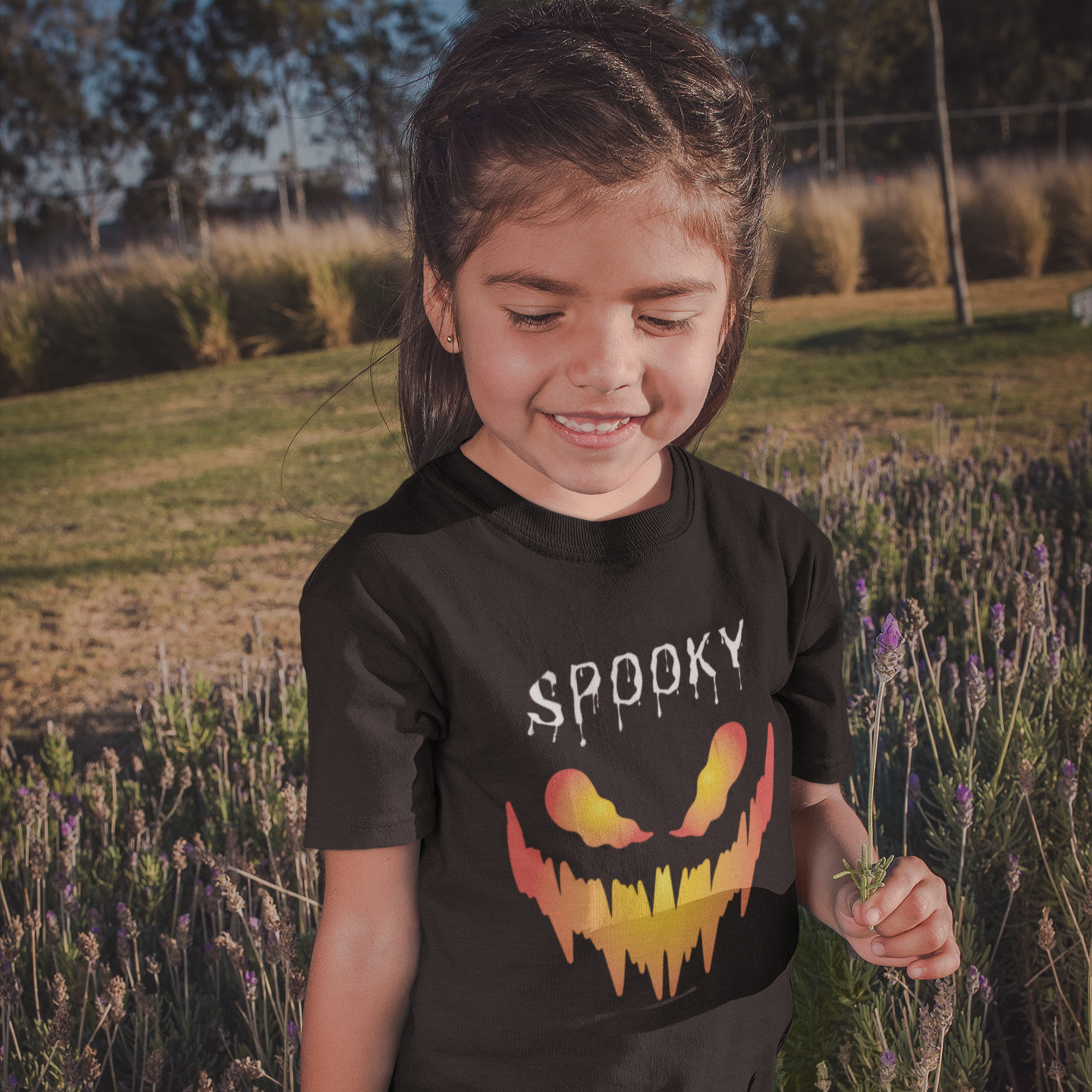 Child wearing a black t-shirt with a Halloween design in a field of tall grass and flowers.