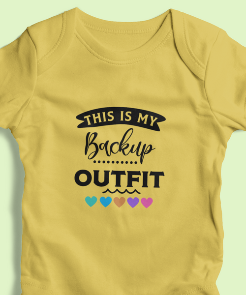 Yellow baby onesie with text "This is my backup outfit" and heart designs on a light green background