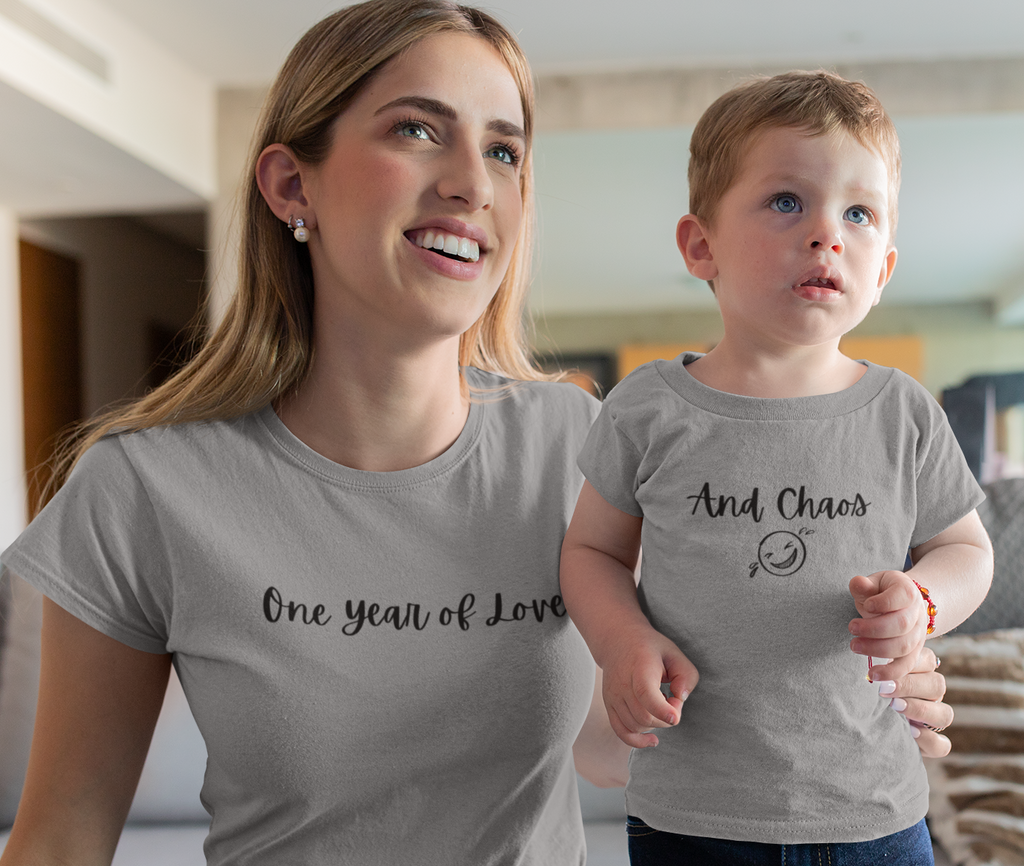 Woman holding a child wearing matching t-shirts with text in a living room.