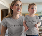 Woman holding a child wearing matching t-shirts with text in a living room.