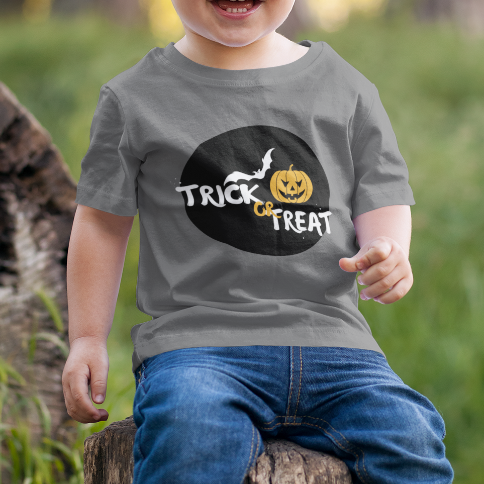 Child wearing a 'Trick or Treat' shirt sitting on a log in a forest