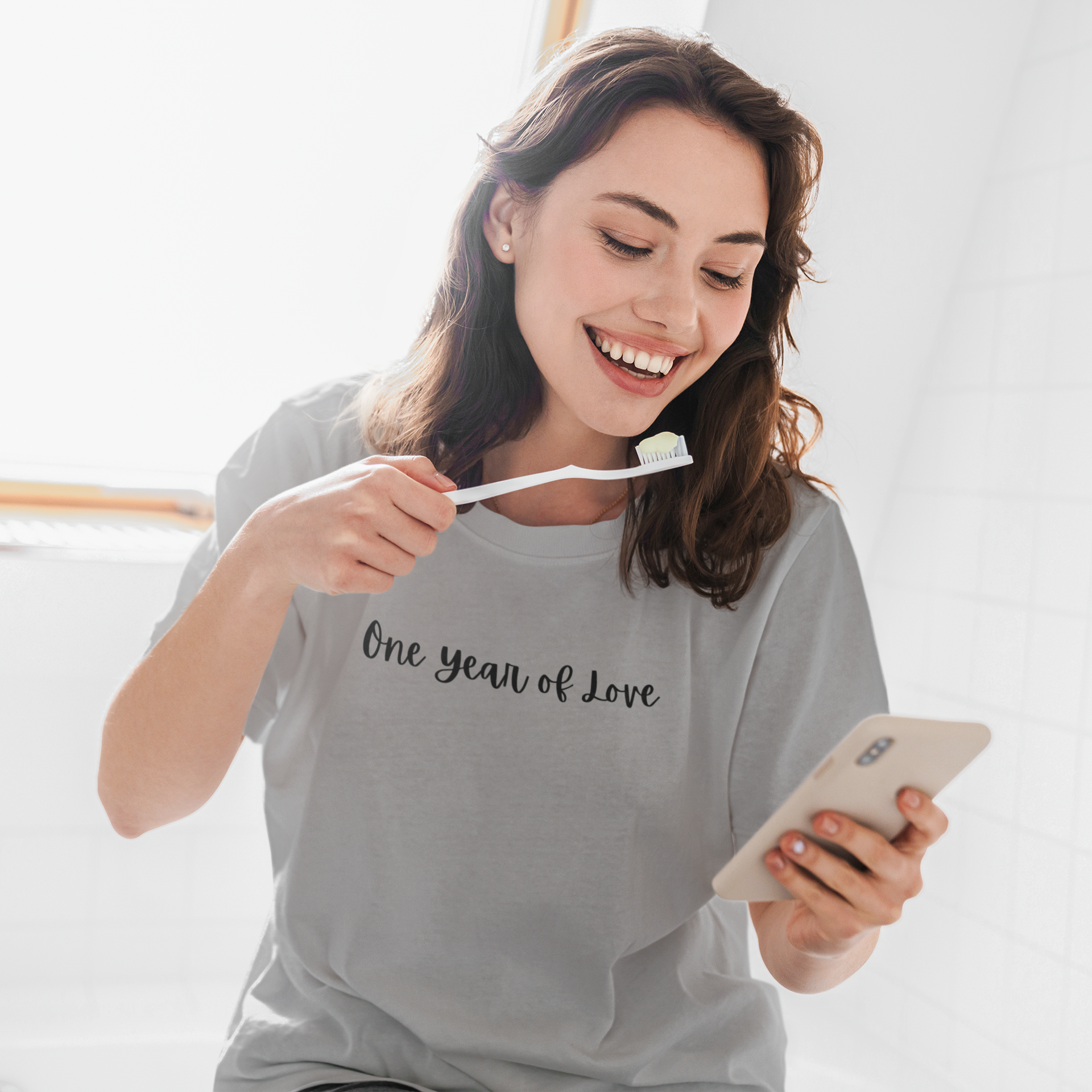 Woman holding a toothbrush and phone, wearing a gray t-shirt with 'One year of Love' text.